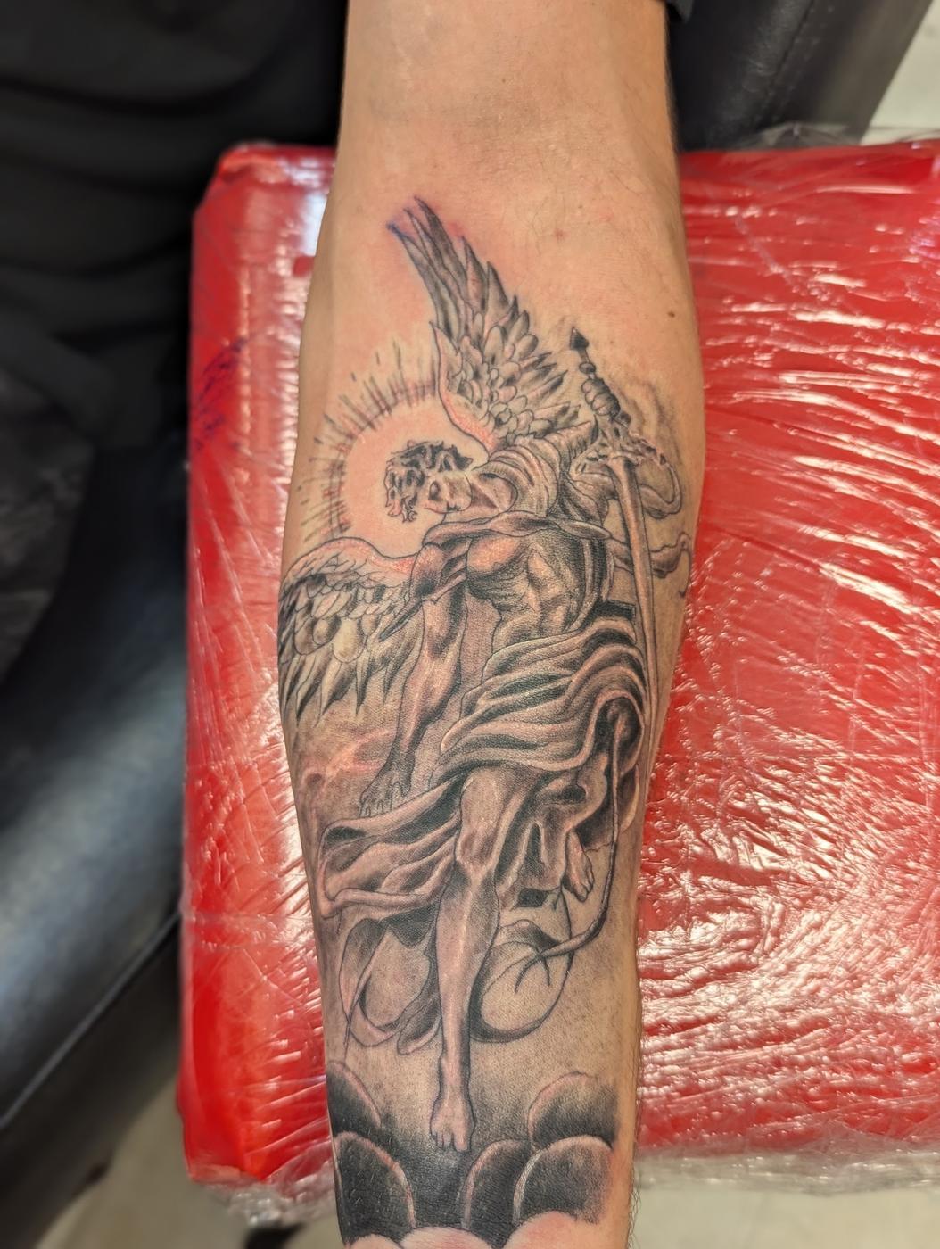 A winged figure tattooed in black and gray ink on a calf, still wrapped in plastic after the session.